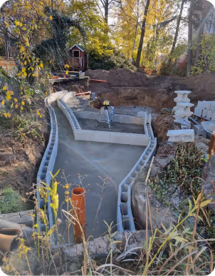 Baustelle mit Betonschalung für einen Teich, umgeben von Bäumen und Garten mit Messgerät in der Mitte.