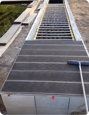 Teilweise verlegter Terrassendielen-Belag mit einem Besen auf der rechten Seite.